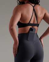 Person wearing a black sports bra and leggings with a phone dropped in concealed pocket of legging