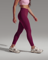 Woman wearing a pink sports bra and maroon leggings on a gray background