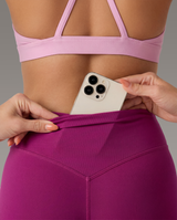 Person wearing a pink sports bra and leggings holding a phone in a concealed pocked in the legging against a gray background