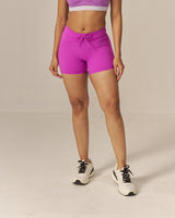 Woman wearing a two tone pink sports bra and magenta shorts set on a beige background