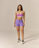 Woman wearing a two toned purple sports bra and lavender shorts set on a beige background