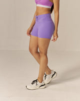Woman wearing a two toned purple sports bra and lavender shorts set on a beige background