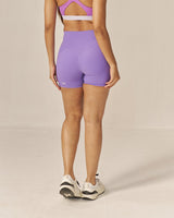 Woman wearing a two toned purple sports bra and lavender shorts set on a beige background