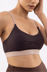 Close-up of a woman wearing a dark brown sports bra with a contrasting beige underband featuring the brand name 'ELA' in white.