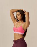 Woman wearing a pink sports bra and maroon shorts on a beige background