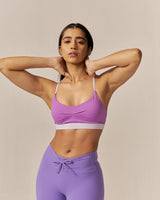 Woman wearing a purple sports bra and leggings against a beige background