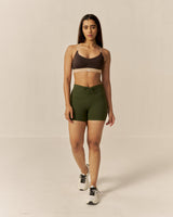 Woman wearing a brown sports bra and green shorts on a beige background