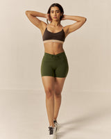 Woman wearing a brown sports bra and green shorts on a beige background