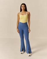 Woman wearing a yellow tank top and blue flared pants on a beige background