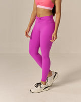 Woman wearing two tone pink sports bra and magenta leggings on a beige background