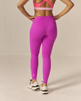 Woman wearing a two tone pink sports bra and magenta leggings on a beige background