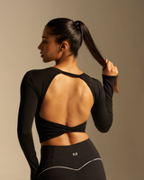 Woman wearing a black athletic outfit with open back design on a beige background