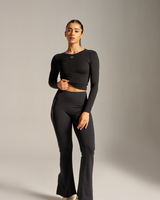 Woman wearing a black long-sleeve top and flared pants on a plain background