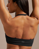 Woman wearing a black sports bra with 'ELA' branding against a neutral background