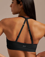 Woman wearing a black sports bra with 'ELA' branding on a beige background