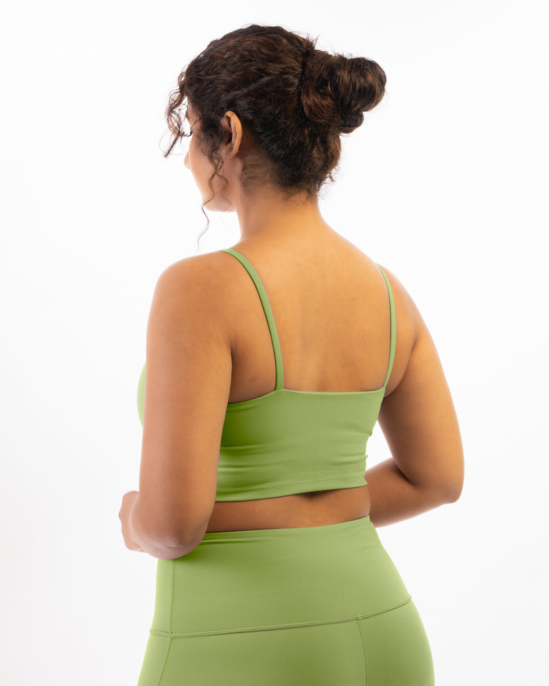 A plus size female model wearing and showing back structure of a matcha-green sports bra, suitable for a variety of workout activities.