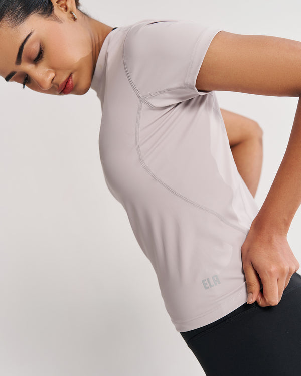 Athletic woman demonstrating the pale grey Performance Tee, a sweat-wicking gym top designed to provide maximum comfort and support during various fitness activities