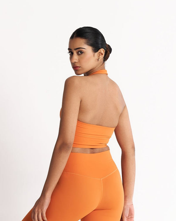 female model showing flattering back design of tangerine orange halter neck sports bra suitable for variety of athletic activities, gym, yoga and workout.