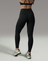 Female athlete wearing a black sports bra and leggings set on a gray background showcasing the back view of legging
