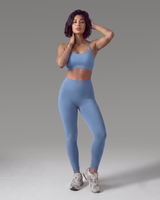 Person wearing blue leggings and a sports bra on a gray background