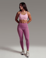 Woman wearing a pink sports bra and leggings on a gray background