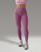 Woman wearing a pink sports bra and leggings on a gray background