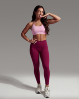 Woman wearing a pink sports bra and maroon leggings posing against a gray background