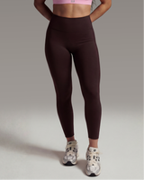 Woman wearing a pink sports bra and brown leggings on a gray background