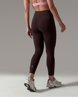 Woman wearing a pink sports bra and brown leggings on a gray background