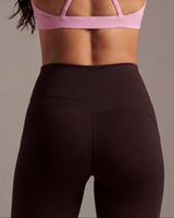 Person wearing a pink sports bra and brown leggings against a neutral background