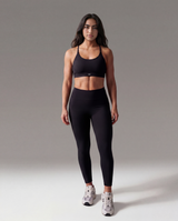 Woman wearing a black sports bra and leggings on a gray background