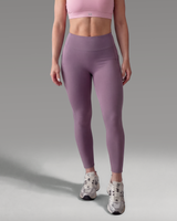 Woman wearing a pink sports bra and purple leggings on a gray background