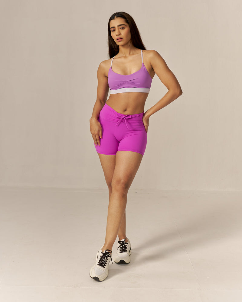 Woman wearing a two tone pink sports bra and magenta shorts set on a beige background