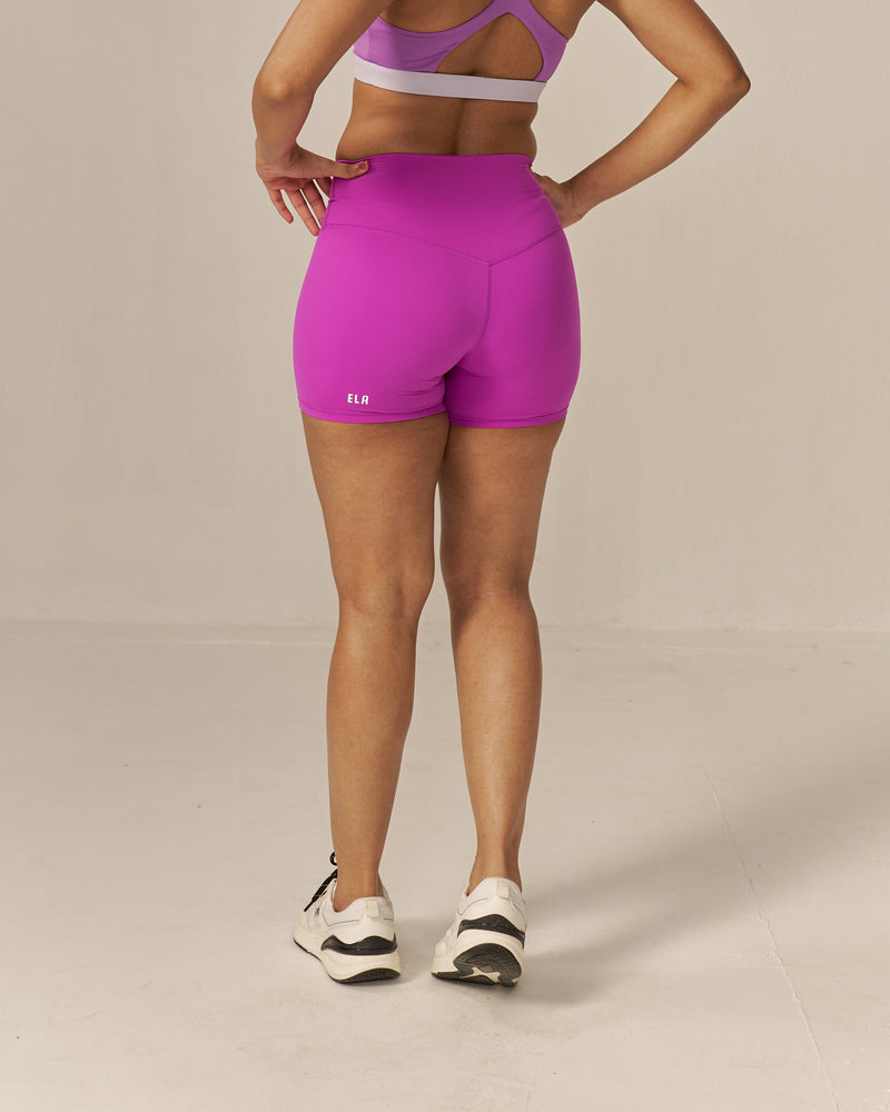 Woman wearing a two tone pink sports bra and magenta shorts set on a beige background