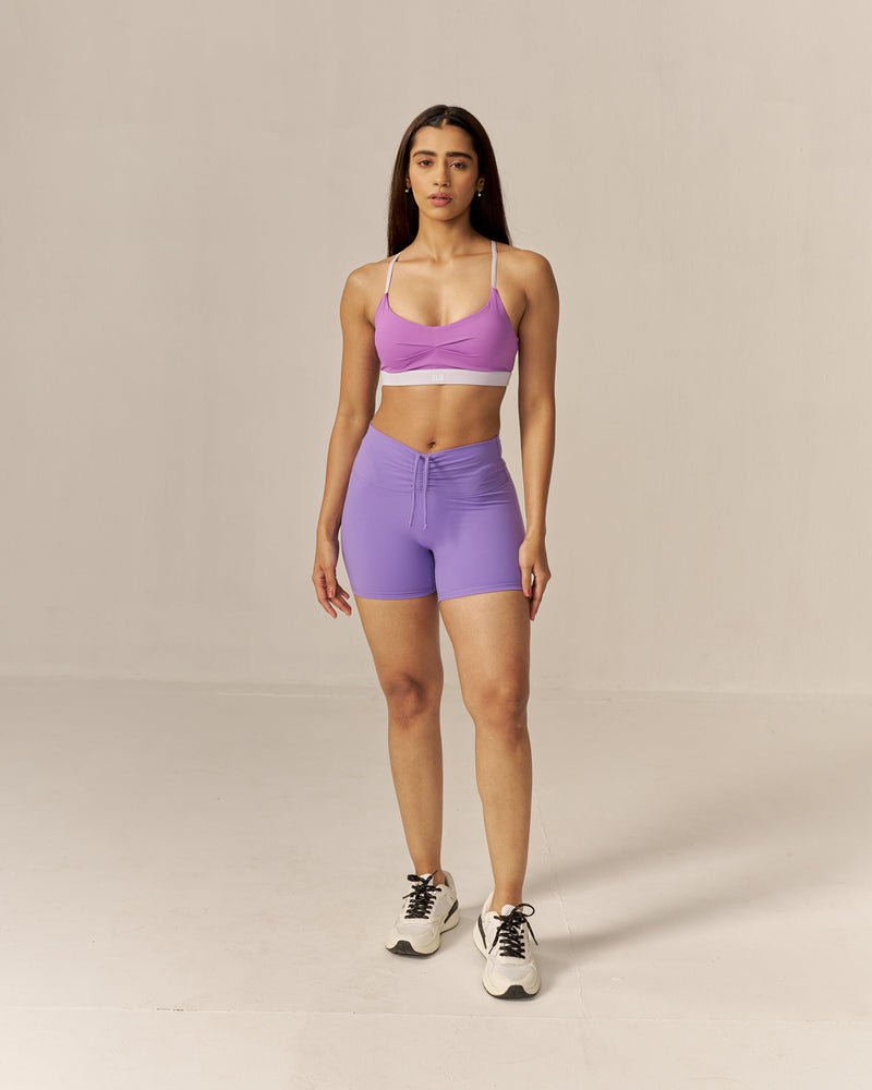 Woman wearing a two toned purple sports bra and lavender shorts set on a beige background