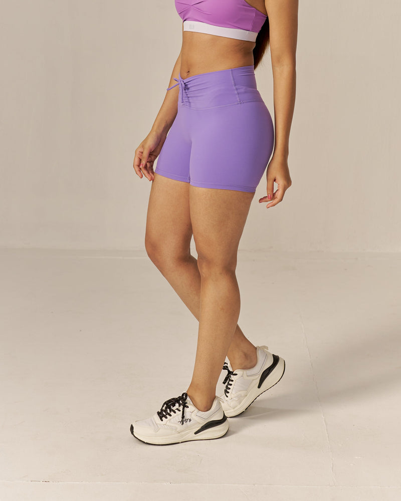 Woman wearing a two toned purple sports bra and lavender shorts set on a beige background