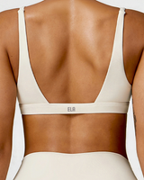 Beige sports bra with 'ELA' brand logo on a plain background