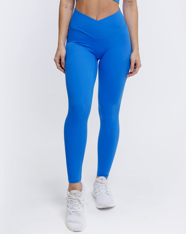 An athletic female model wearing the ButterBod Hourglass Leggings in colour electric blue, highlighting close up of legging. The high-waisted wrap design and V-cut waistband accentuate her curves, while the booty-lifting back seam provides a flattering lift. The legging has a soft matte finish, medium compression, and is made from 4-way stretch fabric for maximum comfort and versatility.