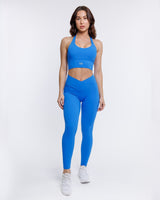 female model in azure blue halter neck sports bra with matching leggings as co-ordinated set suitable for variety of athletic activities, gym, yoga and workout.