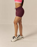 Woman wearing a two tone pink sports bra and maroon brown shorts on a beige background
