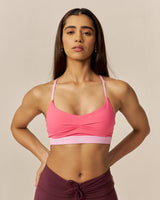 Woman wearing a pink sports bra and maroon shorts on a beige background