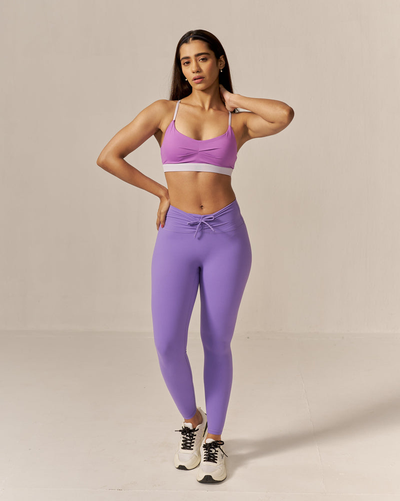 Woman wearing a purple sports bra and leggings on a beige background
