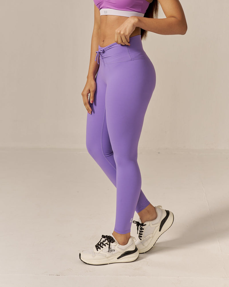 Woman wearing a purple sports bra and leggings on a beige background