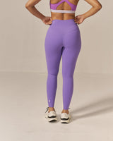Woman wearing a purple sports bra and leggings on a beige background