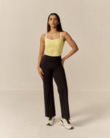Woman wearing a yellow tank top and black pants against a beige background