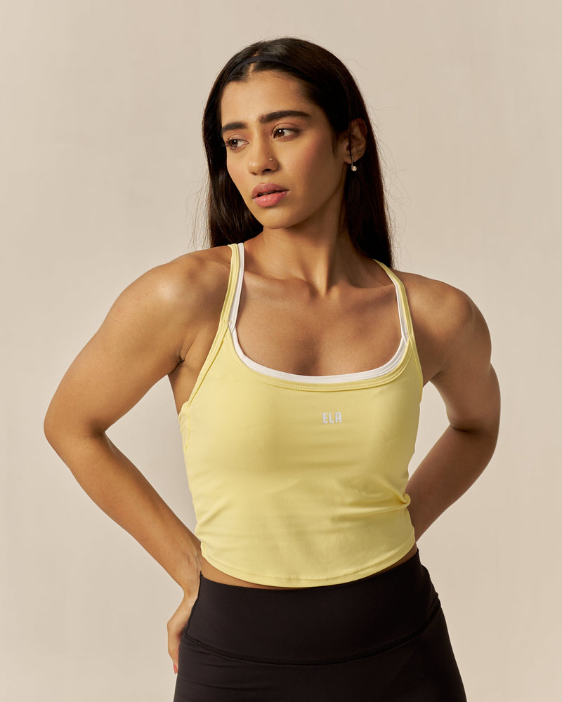 Woman wearing a yellow tank top and black leggings against a beige background
