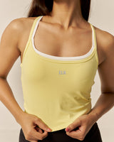Woman wearing a yellow tank top with a visible brand logo against a neutral background