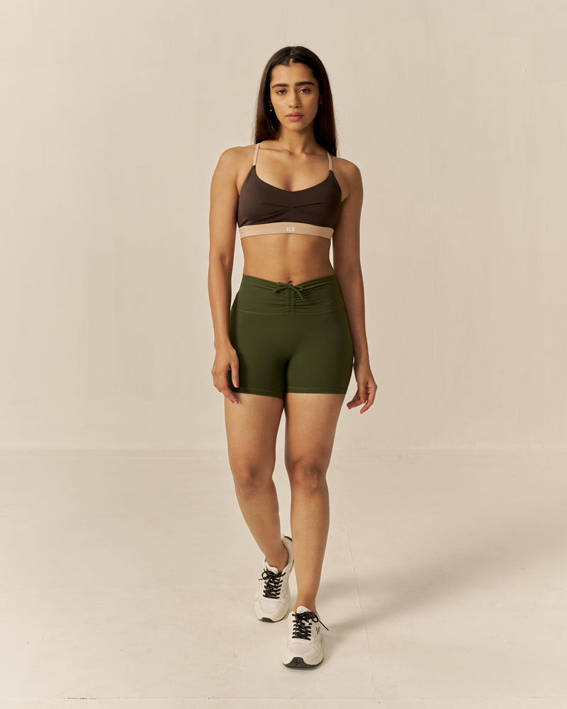 Woman wearing a brown sports bra and green shorts on a beige background