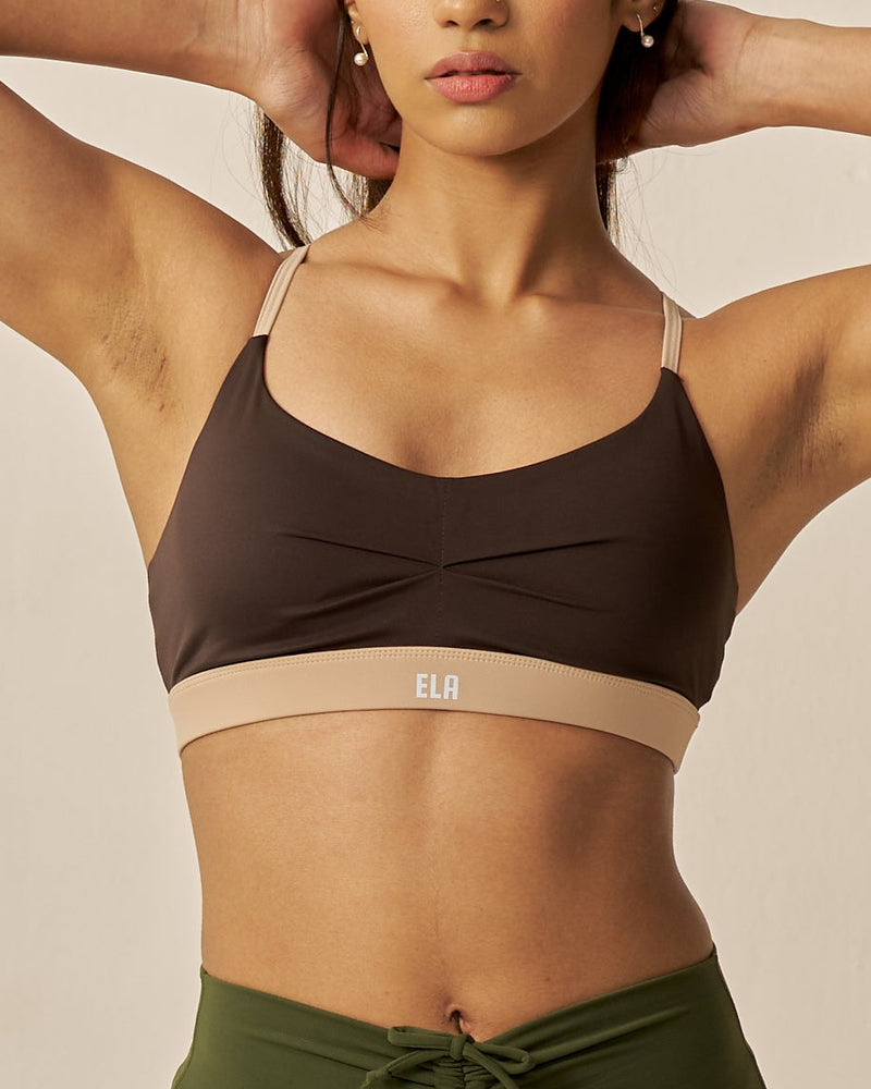 Woman wearing a Dark brown sports bra with beige band and green shorts on a beige background, featuring the brand 'ELA'.