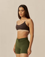 Woman wearing a brown sports bra and green shorts on a beige background